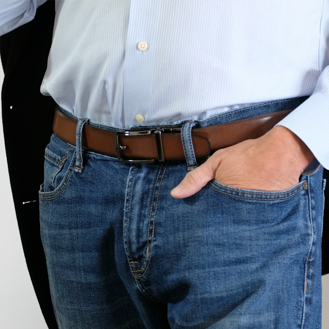 A man wearing the reversible SureFit Belt, brown side facing out, with his hand in his left pocket and thumb hanging out.